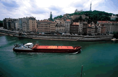 Ein großes Transportschiff irgendwo in Frankreich auf einem Fluss. Im Hintergrund sieht man das Ufer mit Häusern