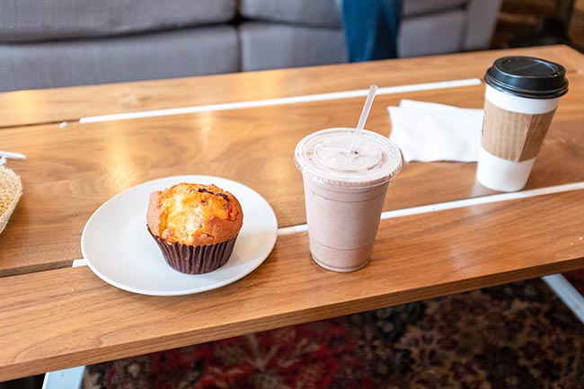 Ein Muffin und ein Kaffee zum mitnehmen stehen auf einem Holztisch bereit zum mitnehmen